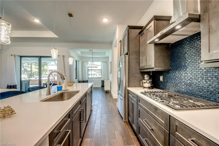 Kitchen with stainless steel appliances, wood finish floors, dark wood finish cabinets, a raised ceiling, and hanging lights