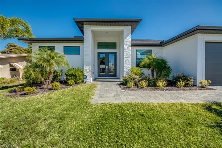 Doorway to property featuring french doors, stucco siding, stone siding, a lawn, and a garage