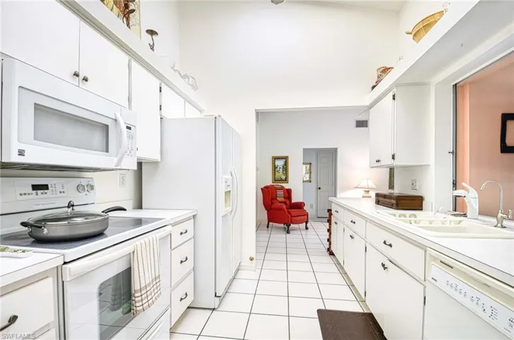 Kitchen featuring white appliances, light countertops, white cabinets, light tile patterned flooring, and a high ceiling