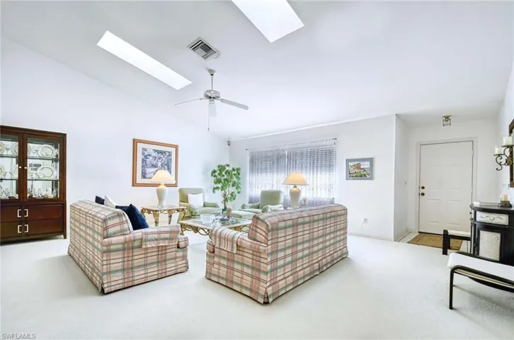Living room with a skylight, light colored carpet, lofted ceiling, and ceiling fan