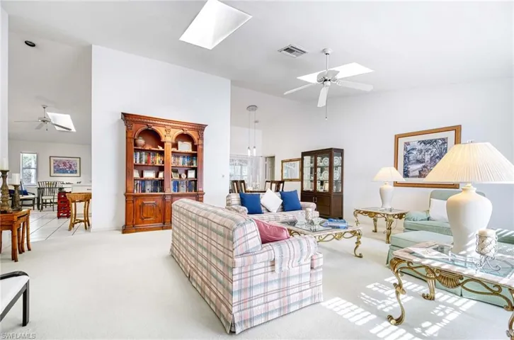 Living room featuring a ceiling fan, a skylight, light colored carpet, and vaulted ceiling