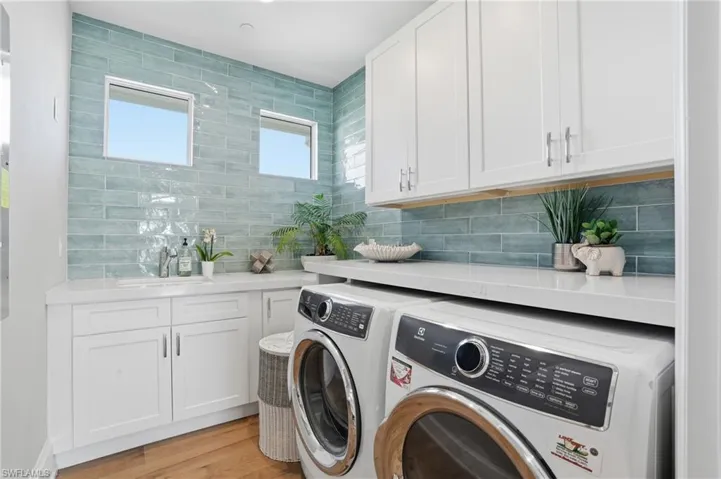 Light and bright laundry room featuring front end washer/dryer, custom cabinetry, utility sink, designer tile, oak hardwood floor.