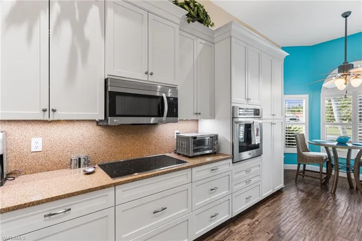 Kitchen featuring appliances with stainless steel finishes, backsplash, a ceiling fan, white cabinets, and dark wood-type flooring