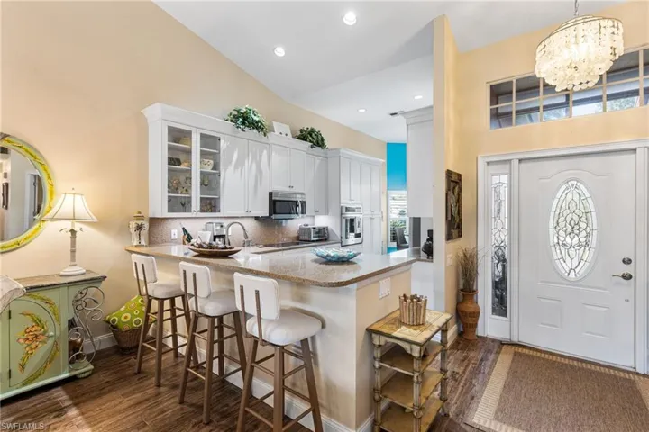 Kitchen featuring dark wood-style floors, glass insert cabinets, a breakfast bar, white cabinets, and recessed lighting