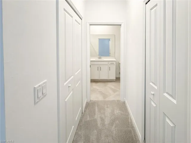 Hall with a sink, light carpet, and baseboards