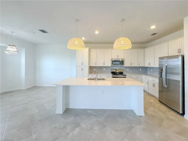 Kitchen featuring appliances with stainless steel finishes, a sink, light countertops, decorative backsplash, and a kitchen island with sink