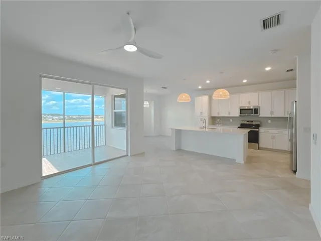 Kitchen featuring appliances with stainless steel finishes, a sink, light countertops, a kitchen island with sink, and white cabinetry