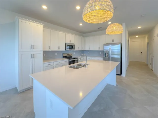 Kitchen featuring stainless steel appliances, a sink, an island with sink, white cabinetry, and light countertops