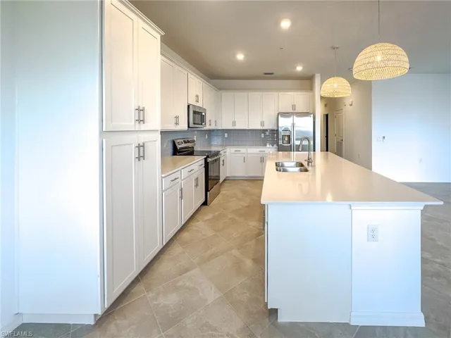Kitchen featuring appliances with stainless steel finishes, a sink, a kitchen island with sink, tasteful backsplash, and white cabinets