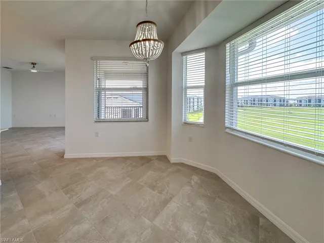 Empty room featuring a chandelier, a ceiling fan, baseboards, and light tile patterned floors