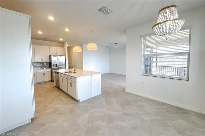 Kitchen with appliances with stainless steel finishes, open floor plan, light countertops, white cabinetry, and a chandelier