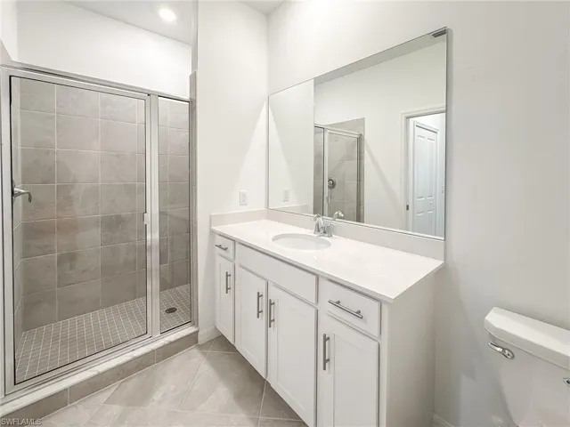 Bathroom featuring a stall shower, toilet, vanity, and tile patterned floors