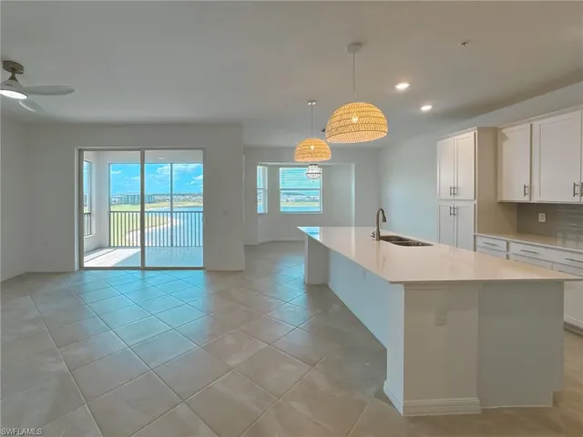 Kitchen featuring a sink, baseboards, light countertops, a kitchen island with sink, and recessed lighting