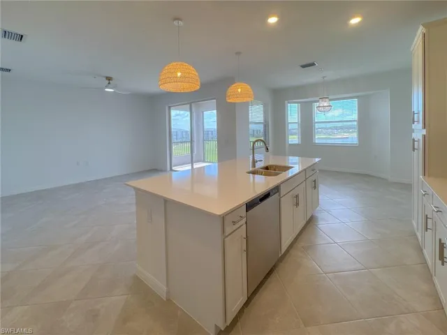 Kitchen with stainless steel dishwasher, a sink, light countertops, baseboards, and light tile patterned floors