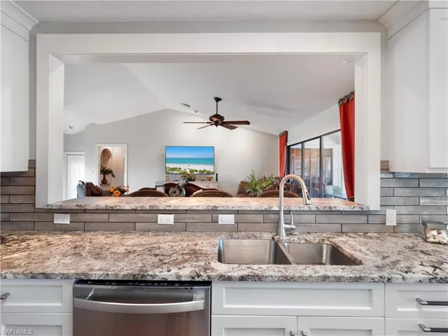 Kitchen with white cabinets, decorative backsplash, lofted ceiling, and sink