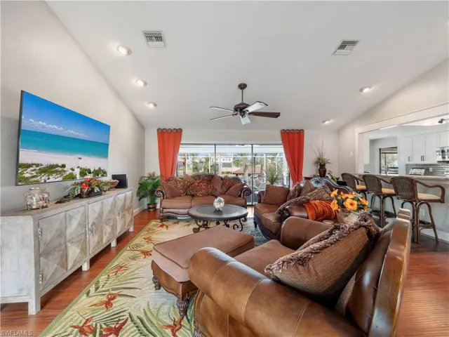 Living room with hardwood / wood-style flooring, vaulted ceiling, and ceiling fan