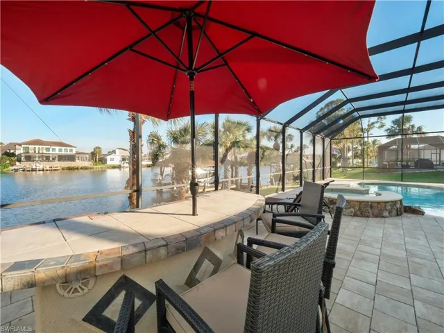 View of patio featuring glass enclosure, a water view, and a pool with hot tub