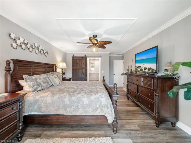 Bedroom with a barn door, light hardwood / wood-style flooring, ceiling fan, and crown molding