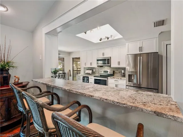 Kitchen featuring white cabinets, a kitchen breakfast bar, light stone countertops, and stainless steel appliances