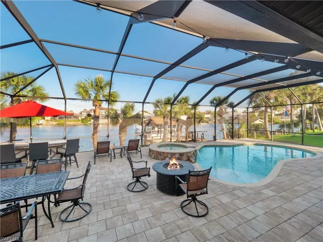 View of swimming pool featuring a patio, a water view, glass enclosure, and an outdoor fire pit