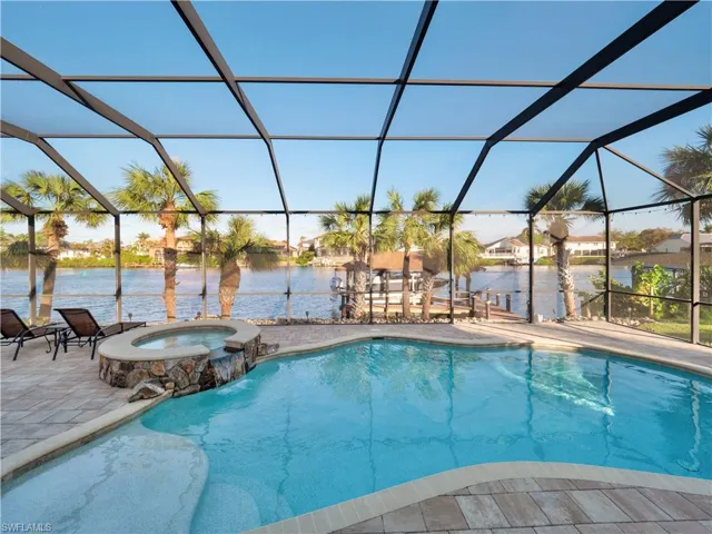 View of swimming pool featuring glass enclosure, a water view, an in ground hot tub, and a patio