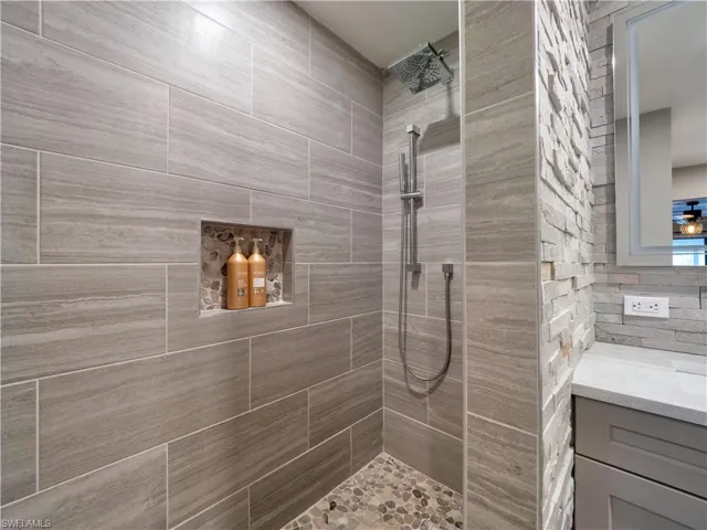 Bathroom featuring vanity, a tile shower, and tile walls