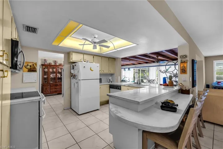 Kitchen with white appliances, light countertops, a peninsula, a kitchen breakfast bar, and ceiling fan