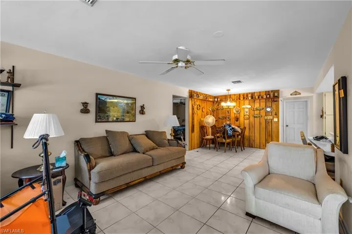 Living room featuring ceiling fan, suspended lighting, and wood walls