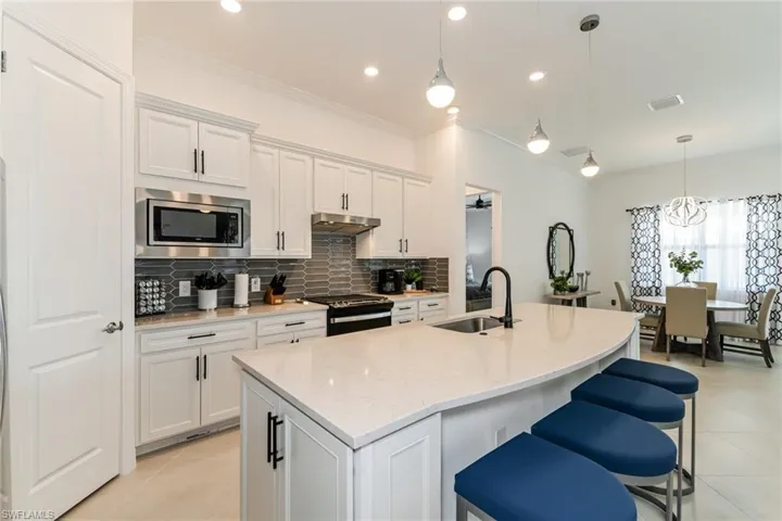 Kitchen with a breakfast bar, ornamental molding, light stone counters, hanging light fixtures, and an island with sink
