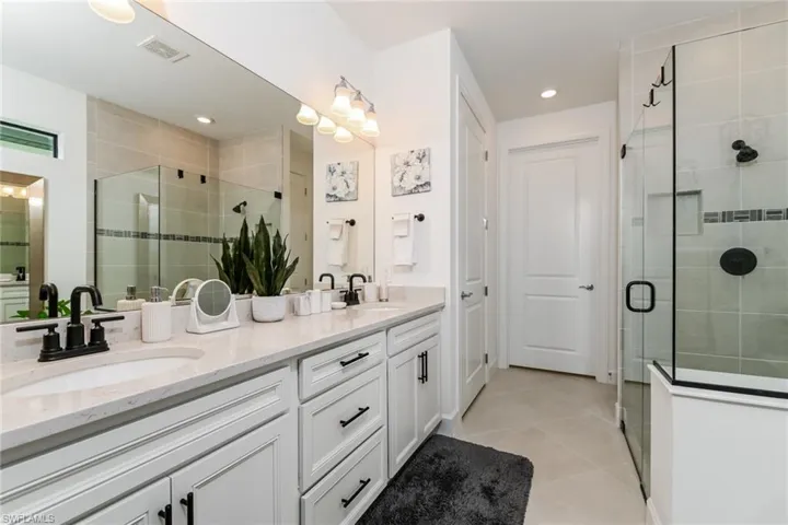 Full bath with double vanity, a shower stall, and light tile patterned flooring