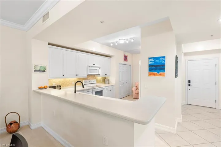 Kitchen featuring light countertops, tasteful backsplash, white appliances, visible vents, and ornamental molding