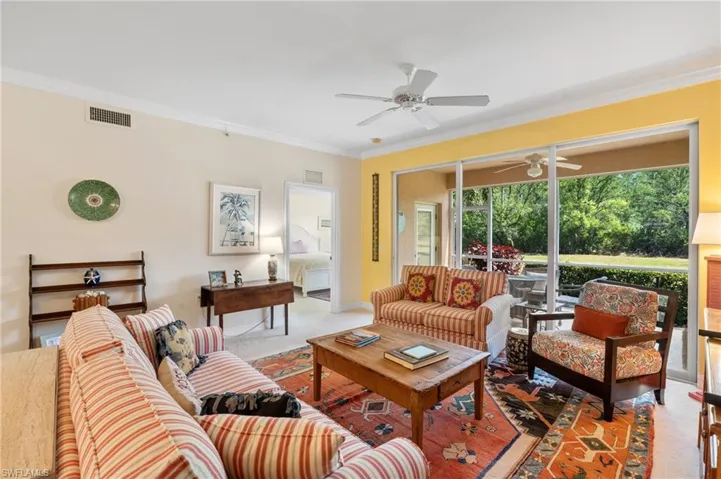 Living room with carpet flooring, ceiling fan, visible vents, and ornamental molding