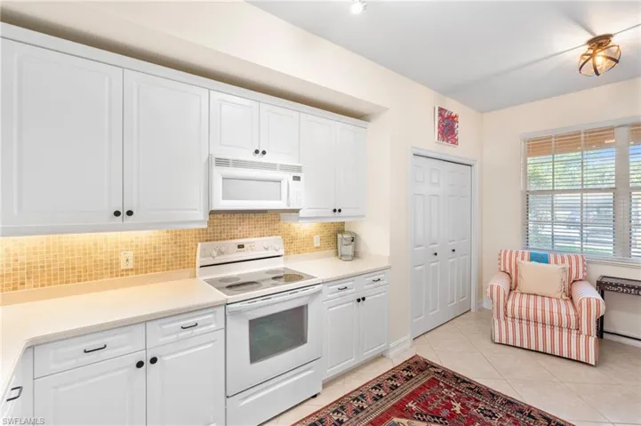 Kitchen featuring light tile patterned flooring, white cabinetry, backsplash, and white appliances