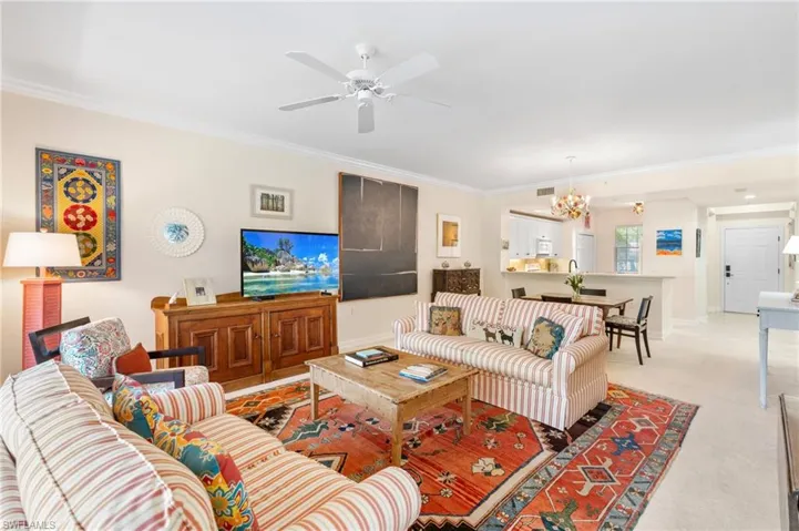 Living room featuring light colored carpet, crown molding, baseboards, and ceiling fan with notable chandelier