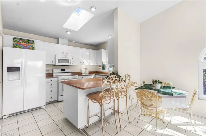 Kitchen with a skylight, white appliances, a breakfast bar, and white cabinets