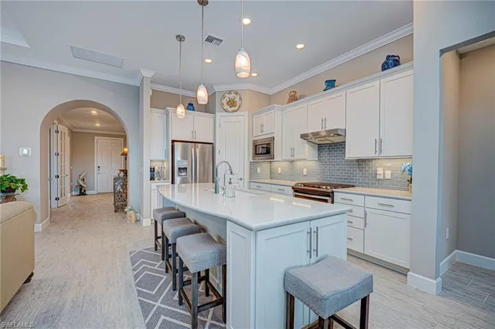 Kitchen featuring stainless steel appliances, arched walkways, a breakfast bar area, white cabinetry, and a kitchen island with sink