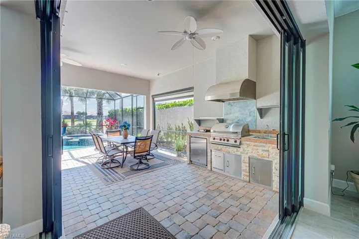 View of patio with a sunroom, ceiling fan, an outdoor kitchen / dining area, glass enclosure, and a pool with connected hot tub