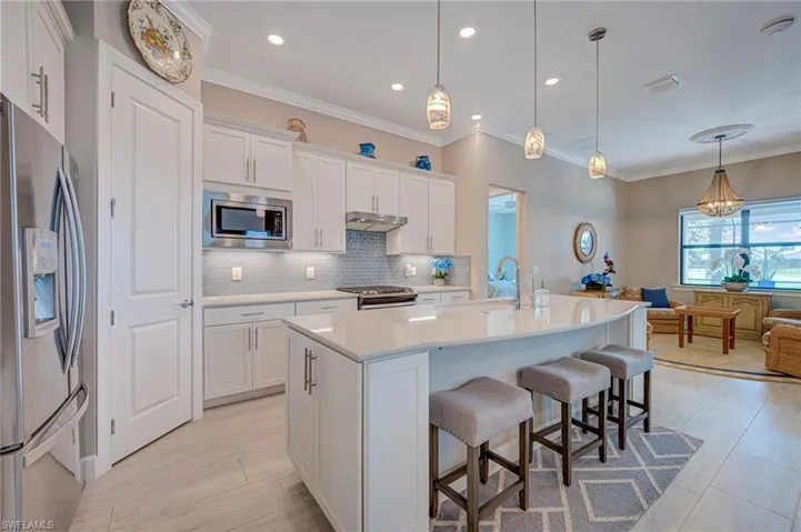 Kitchen with a center island with sink, stainless steel appliances, ornamental molding, a kitchen breakfast bar, and white cabinetry