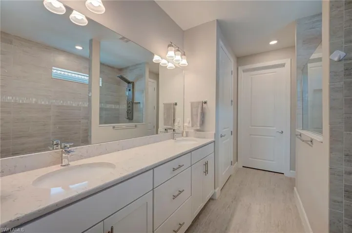 Bathroom featuring a walk in shower, double vanity, light wood finished floors, and recessed lighting