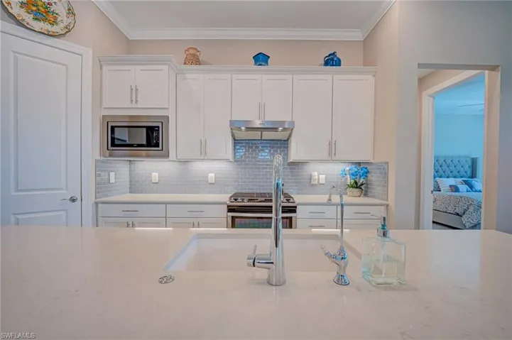 Kitchen with white cabinets, stainless steel appliances, light stone countertops, tasteful backsplash, and ornamental molding