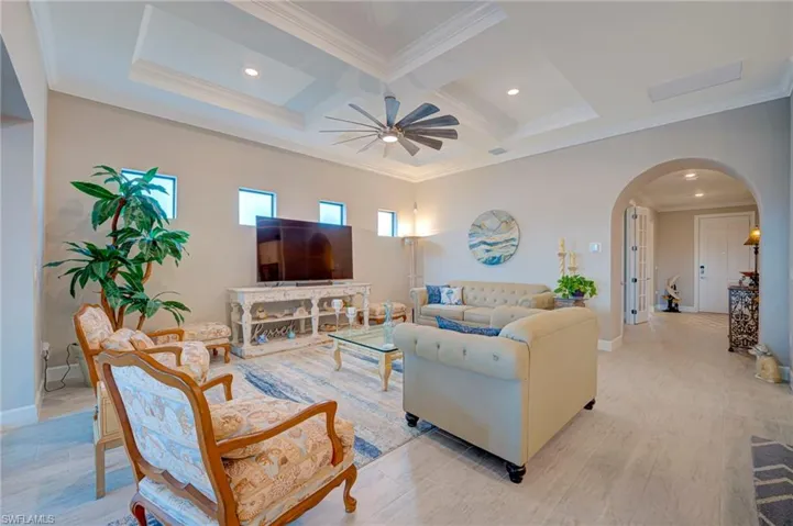 Living area featuring crown molding, arched walkways, coffered ceiling, a ceiling fan, and recessed lighting