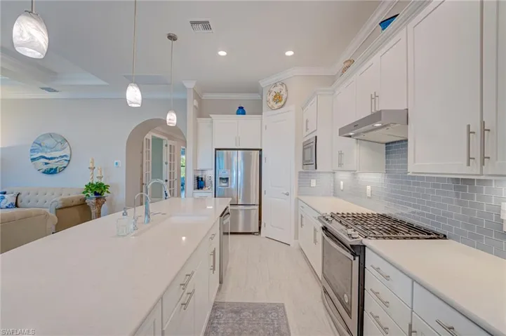 Kitchen featuring stainless steel appliances, white cabinets, arched walkways, ornamental molding, and decorative light fixtures