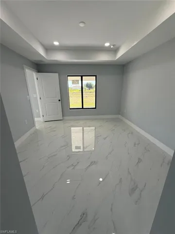 Spare room with marble finish floor, recessed lighting, a tray ceiling, and baseboards