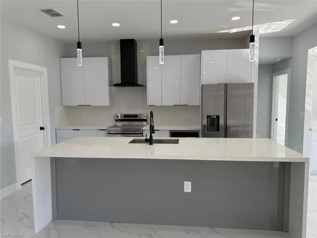 Kitchen with a large island, modern cabinets, a sink, appliances with stainless steel finishes, and wall chimney range hood