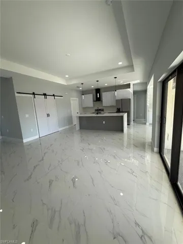 Unfurnished living room featuring a raised ceiling, marble finish floor, a sink, recessed lighting, and baseboards