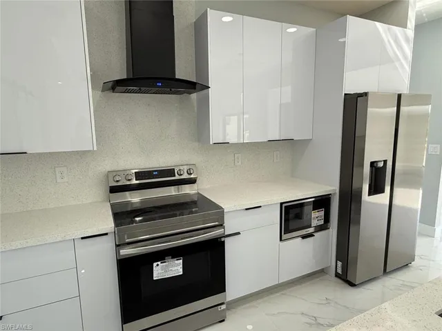 Kitchen with modern cabinets, marble finish floor, white cabinetry, stainless steel appliances, and wall chimney range hood