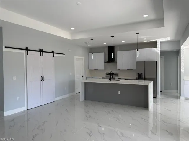 Kitchen with modern cabinets, a barn door, stainless steel fridge, light countertops, and extractor fan