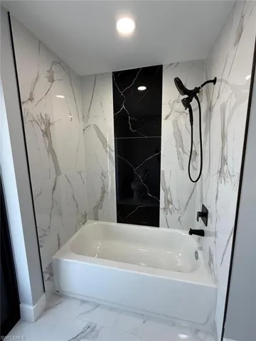 Full bathroom featuring stone wall, marble finish floor, and shower / bath combination