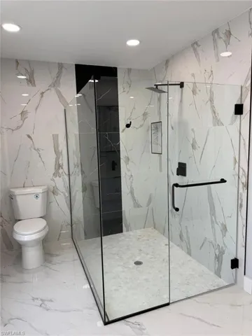 Bathroom featuring stone wall, a marble finish shower, recessed lighting, toilet, and marble finish floor