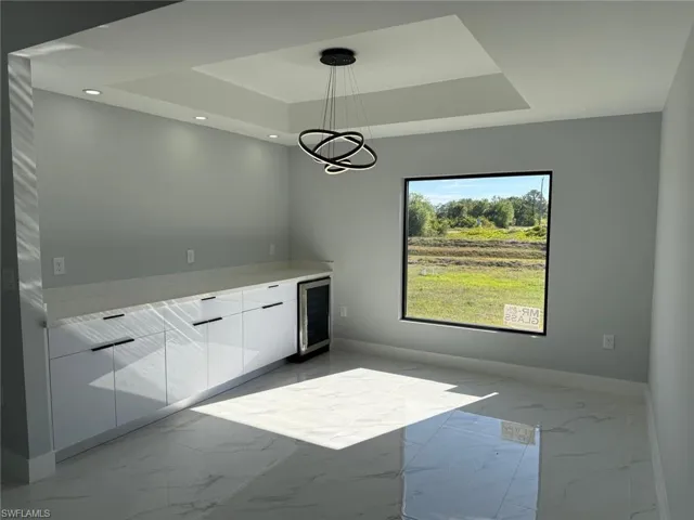 Unfurnished dining area featuring a tray ceiling, beverage cooler, marble finish floor, and baseboards